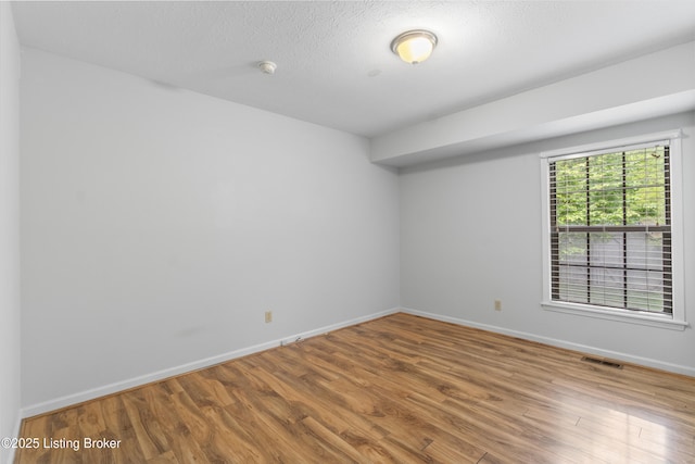 unfurnished room with a textured ceiling, baseboards, visible vents, and wood finished floors