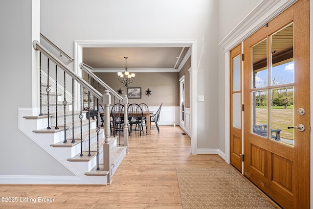 foyer entrance featuring an inviting chandelier, crown molding, stairs, wood finished floors, and a wainscoted wall