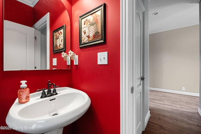 bathroom featuring a sink, baseboards, crown molding, and wood finished floors