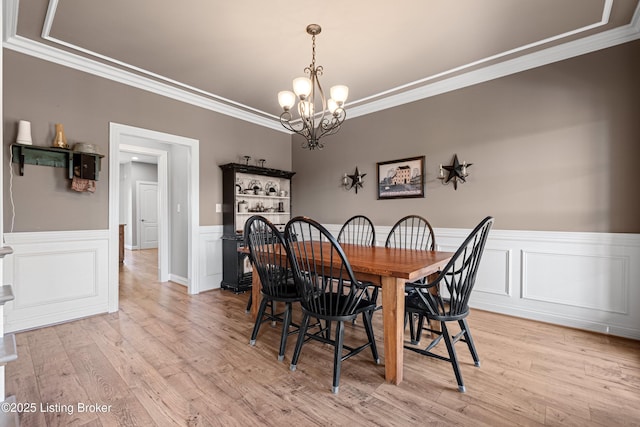 dining room with light wood-type flooring, an inviting chandelier, ornamental molding, and a wainscoted wall