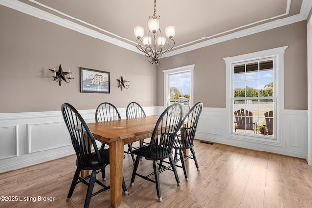 dining area featuring crown molding, a wainscoted wall, light wood finished floors, and a notable chandelier
