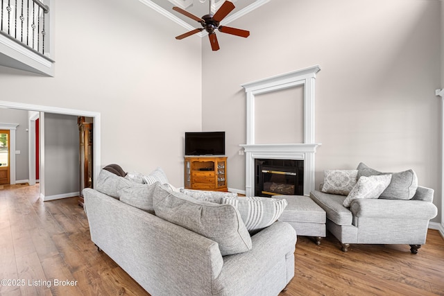 living area with a high ceiling, a fireplace, a ceiling fan, wood finished floors, and ornamental molding