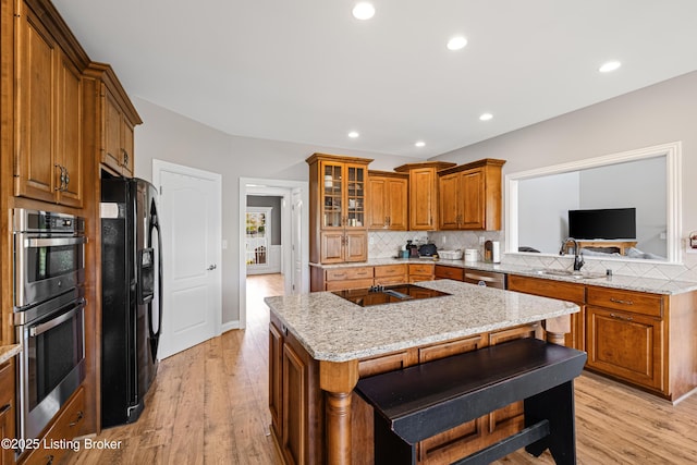 kitchen featuring a sink, light wood finished floors, brown cabinetry, backsplash, and black appliances