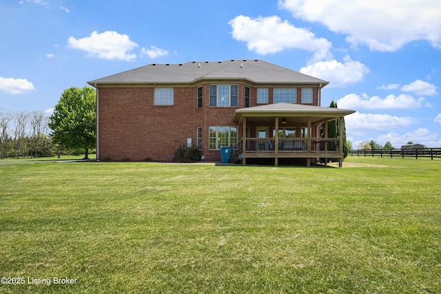 rear view of property with a lawn, brick siding, and fence