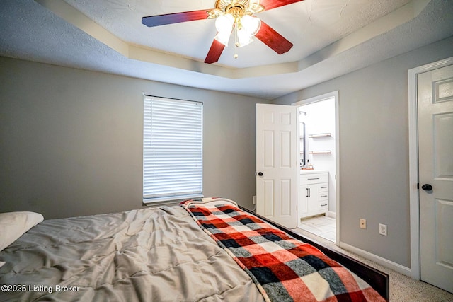 bedroom with baseboards, a raised ceiling, connected bathroom, light carpet, and ceiling fan