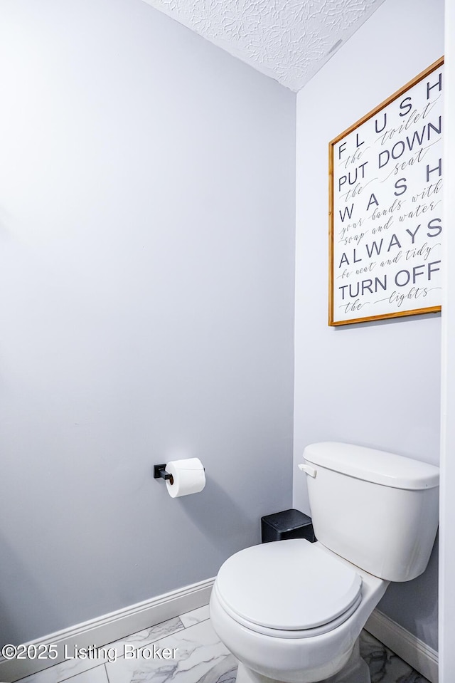 bathroom featuring marble look tiles, baseboards, toilet, and a textured ceiling