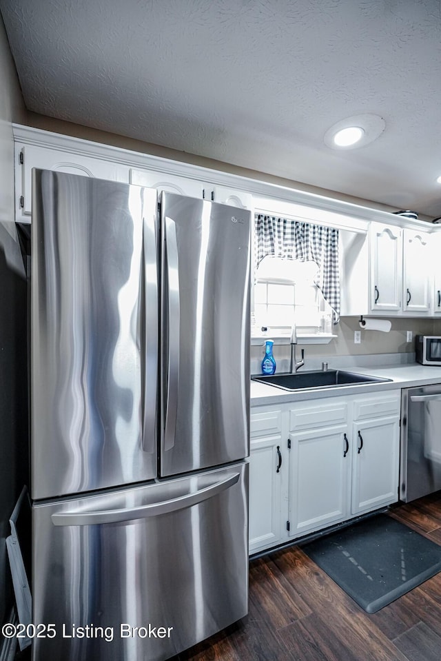 kitchen featuring stainless steel appliances, a sink, white cabinetry, dark wood finished floors, and a textured ceiling