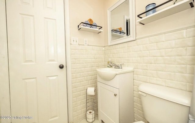 half bathroom with toilet, vanity, wainscoting, and tile walls