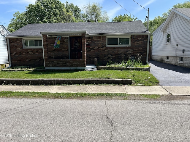 view of front of property featuring brick siding, roof with shingles, and a front yard