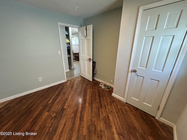 unfurnished bedroom with baseboards and dark wood-type flooring