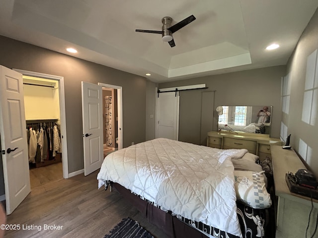 bedroom with recessed lighting, wood finished floors, a tray ceiling, a spacious closet, and a closet