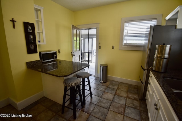 kitchen featuring a peninsula, a breakfast bar, baseboards, white cabinetry, and stainless steel appliances