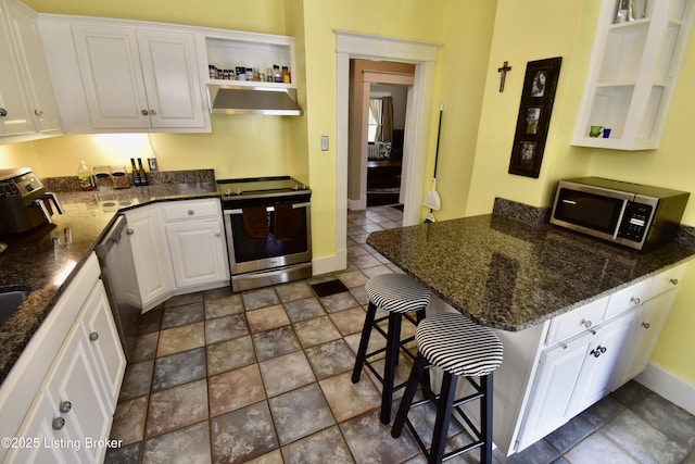 kitchen with open shelves, a breakfast bar, wall chimney range hood, white cabinets, and appliances with stainless steel finishes