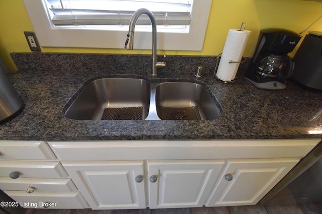 interior details featuring white cabinetry, a sink, and dark stone countertops