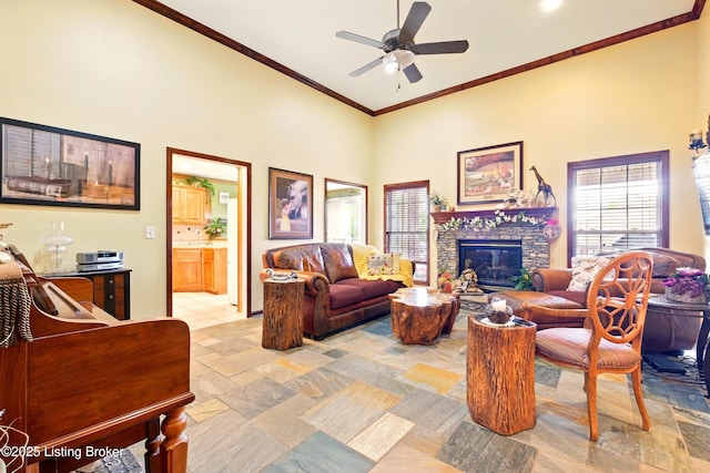 living area featuring a fireplace, crown molding, ceiling fan, and a high ceiling