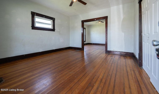 spare room with dark wood-type flooring, a ceiling fan, and baseboards