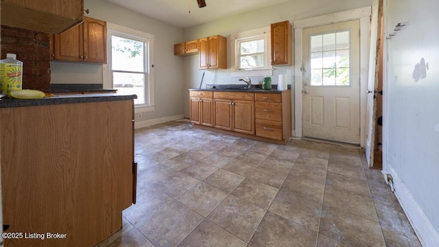 kitchen featuring brown cabinetry, dark countertops, ceiling fan, a sink, and baseboards