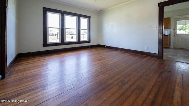 empty room with baseboards, crown molding, and dark wood-type flooring