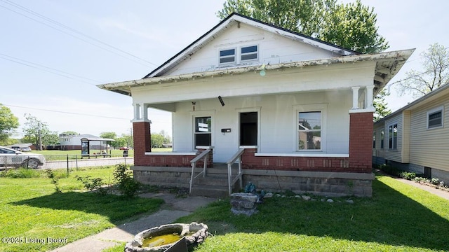 bungalow-style home featuring a porch, a front lawn, fence, and brick siding
