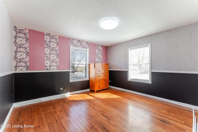 unfurnished room featuring baseboards, a healthy amount of sunlight, hardwood / wood-style floors, and wallpapered walls