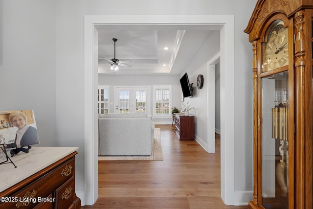 hall featuring light wood-type flooring, recessed lighting, a raised ceiling, and baseboards