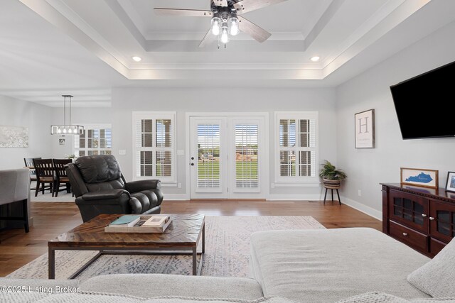 living area featuring crown molding, ceiling fan with notable chandelier, wood finished floors, and a tray ceiling