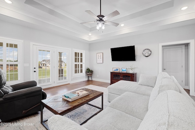 living area featuring a raised ceiling, light wood-style flooring, recessed lighting, baseboards, and a ceiling fan