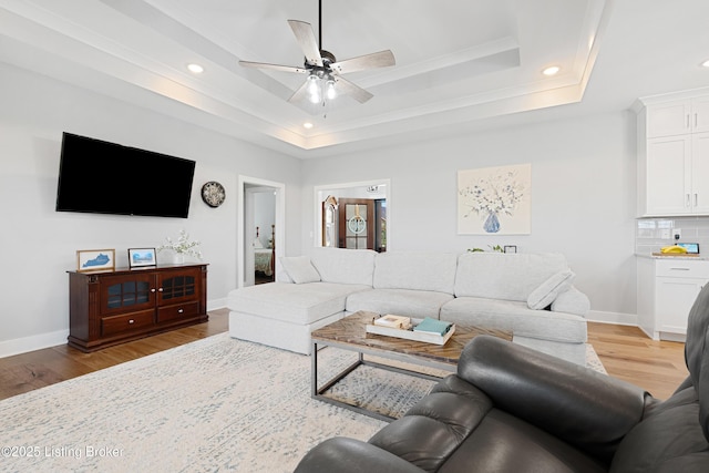 living area with recessed lighting, ornamental molding, a raised ceiling, and light wood-type flooring
