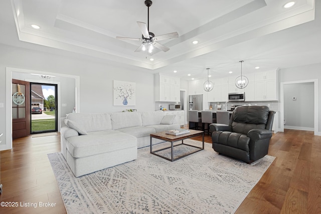 living area featuring a raised ceiling, a ceiling fan, recessed lighting, and wood finished floors