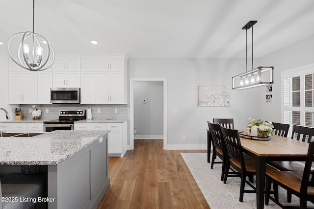kitchen with decorative backsplash, baseboards, a notable chandelier, light wood-style floors, and stainless steel appliances