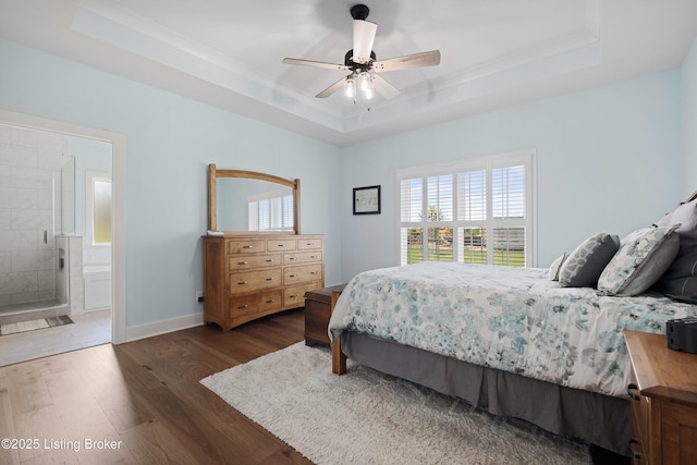 bedroom featuring a ceiling fan, wood finished floors, baseboards, ensuite bathroom, and a tray ceiling