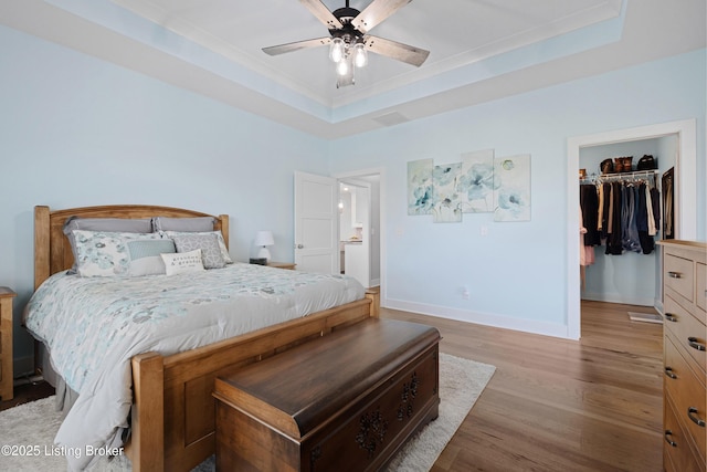 bedroom featuring baseboards, a walk in closet, light wood-type flooring, a tray ceiling, and a ceiling fan