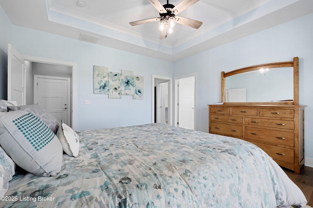 bedroom with visible vents, ceiling fan, wood finished floors, and a tray ceiling
