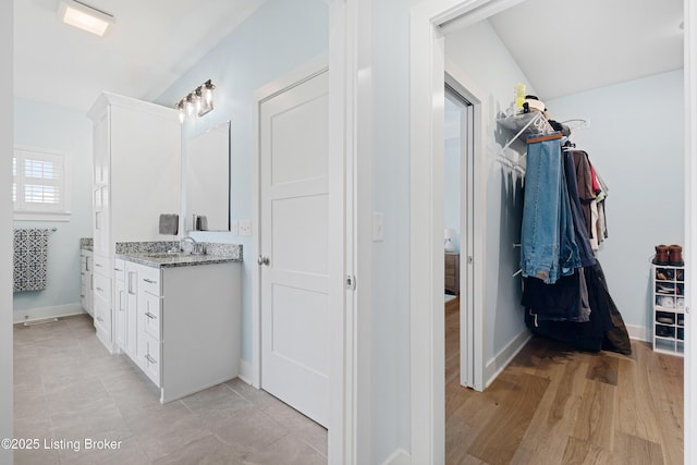bathroom with a walk in closet, baseboards, and vanity