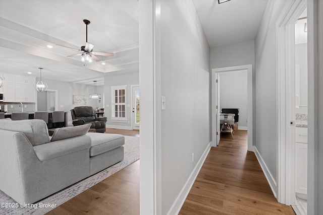 hallway featuring crown molding, wood finished floors, baseboards, a tray ceiling, and recessed lighting