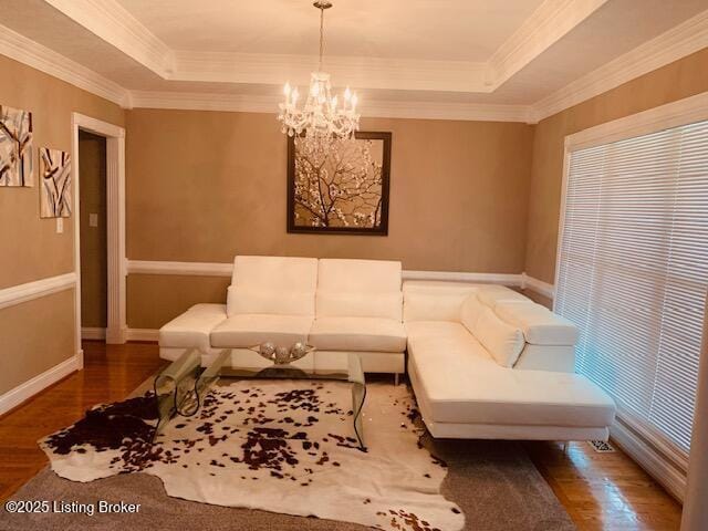 living area with a raised ceiling, ornamental molding, wood finished floors, and a chandelier