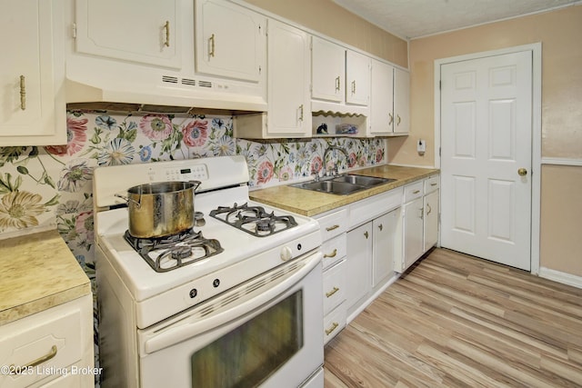 kitchen featuring a sink, light countertops, gas range gas stove, light wood-style flooring, and under cabinet range hood