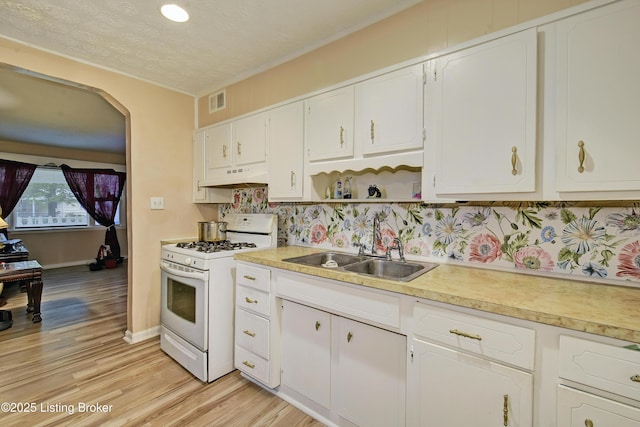 kitchen featuring visible vents, white gas stove, light countertops, under cabinet range hood, and a sink