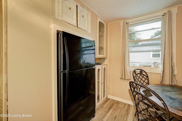 kitchen with a textured ceiling, light wood-type flooring, baseboards, freestanding refrigerator, and glass insert cabinets