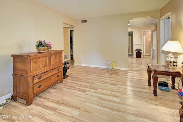 living area with arched walkways, baseboards, visible vents, and light wood-style flooring