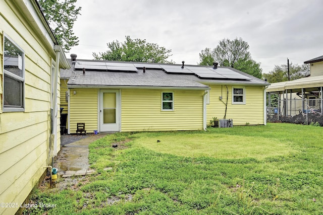 back of house featuring a lawn, cooling unit, roof with shingles, and solar panels