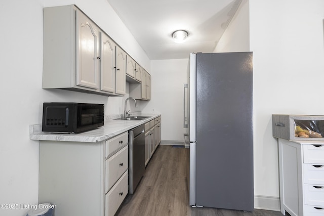 kitchen featuring wood finished floors, baseboards, light countertops, a sink, and appliances with stainless steel finishes
