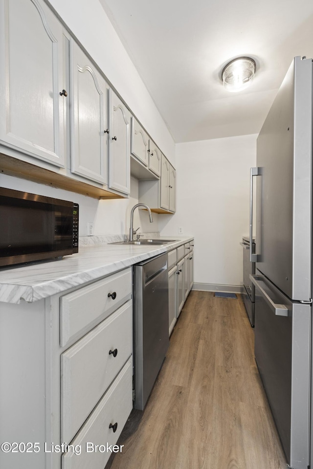 kitchen with a sink, light wood finished floors, appliances with stainless steel finishes, and light stone countertops