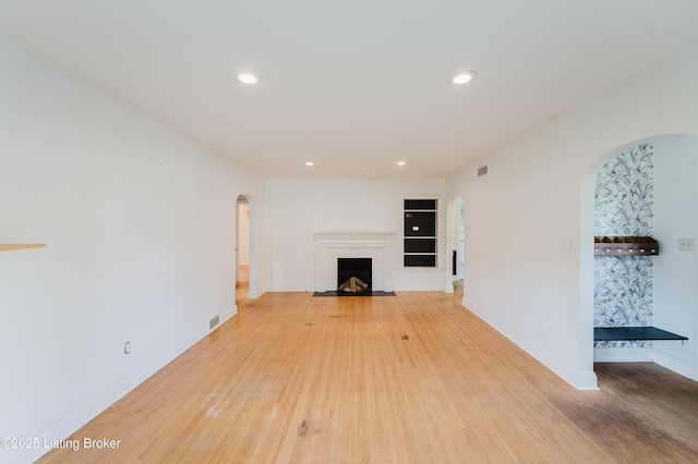unfurnished living room featuring light wood-style flooring, recessed lighting, baseboards, a fireplace with flush hearth, and arched walkways