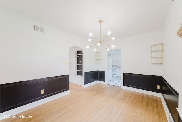 unfurnished dining area featuring light wood finished floors, a notable chandelier, visible vents, arched walkways, and built in shelves