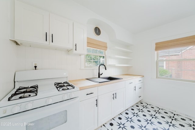 kitchen with white cabinets, white gas range oven, open shelves, and a sink