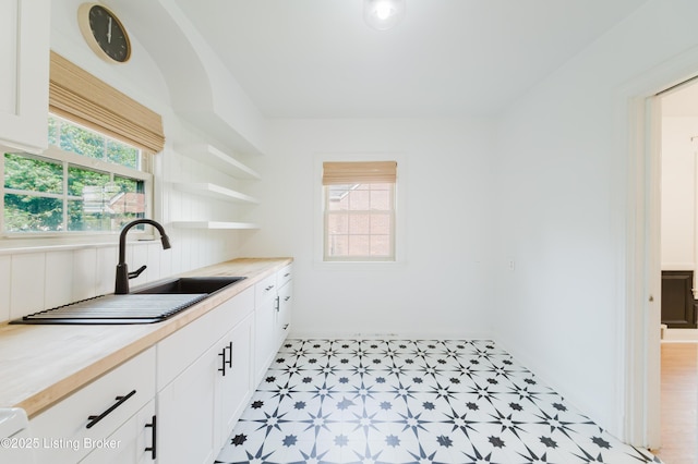 kitchen with a sink, open shelves, white cabinets, light floors, and light countertops