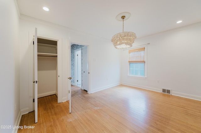 unfurnished bedroom featuring an inviting chandelier, crown molding, light wood-type flooring, and visible vents