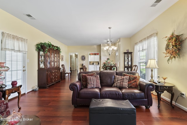 living area with visible vents, baseboards, wood finished floors, and a chandelier