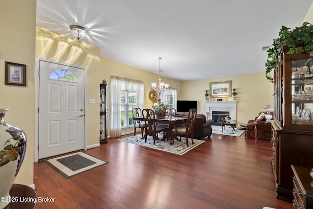 dining space featuring visible vents, dark wood-style flooring, a glass covered fireplace, baseboards, and a chandelier